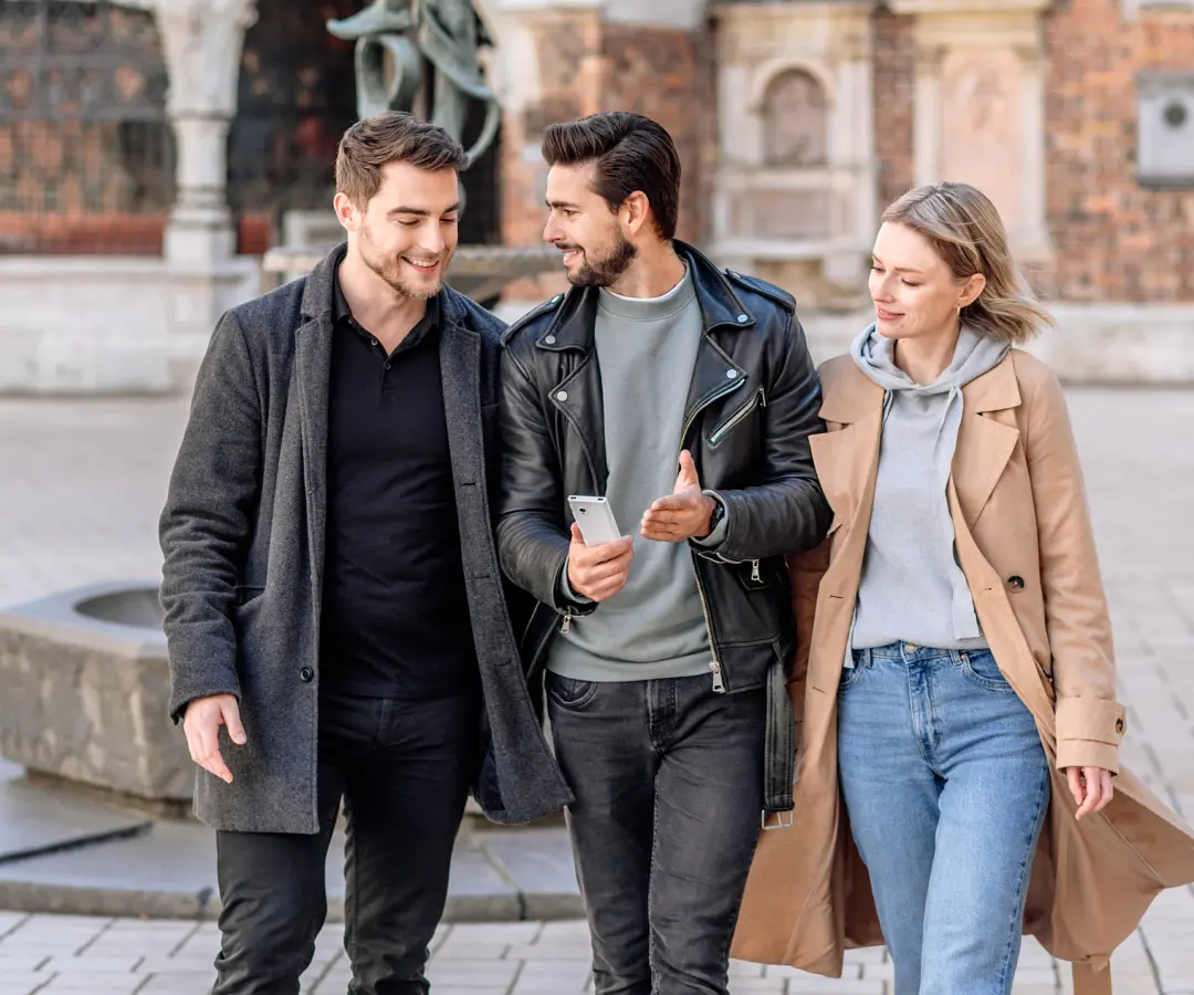 Un homme tient un traducteur à la main et est entouré d’amis. En arrière-plan, l’architecture historique est visible